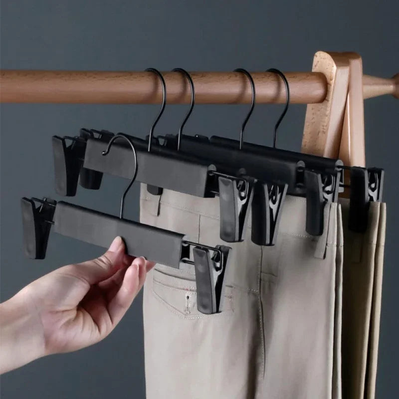 A hand is hanging adjustable black clothes hangers on a wooden rod, with a beige fabric item nearby.