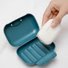 A hand is opening a teal portable travel soap box to dispense white soap.