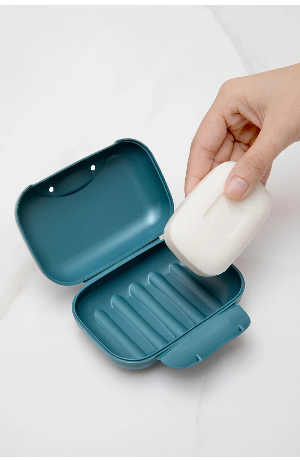 A hand is opening a teal portable travel soap box to dispense white soap.