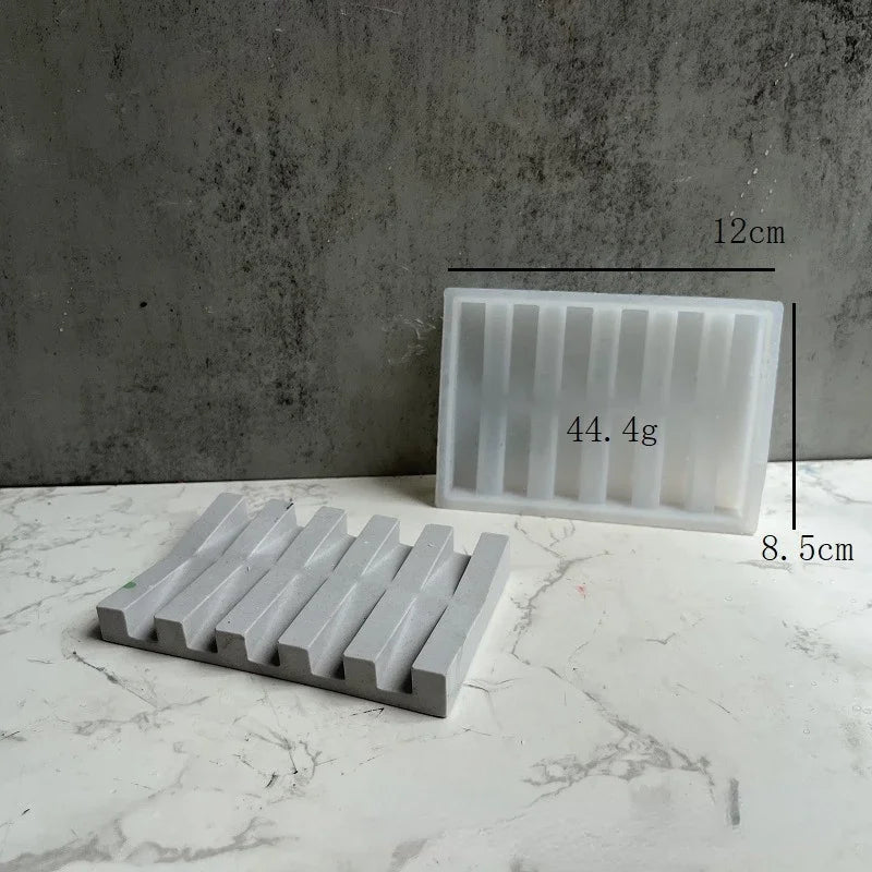 Weiße Silikon-Seifenspeicherschale mit parallelen Rillen neben einem rechteckigen weißen Formteil.