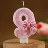 Pink glitter number 8 birthday candle with a pink bow on a wooden surface