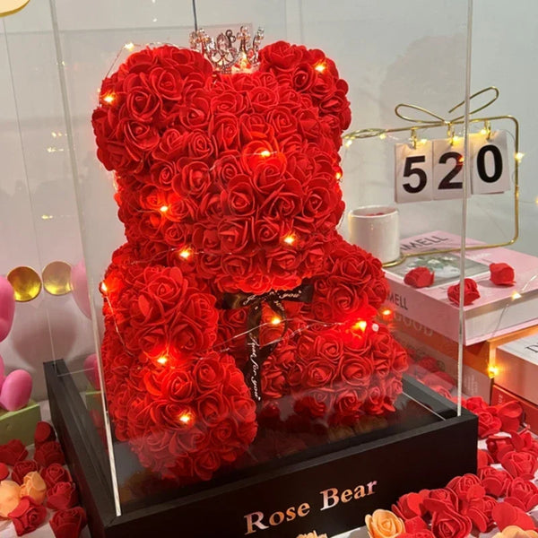 A vibrant red rose bear crafted from fabric and adorned with twinkling lights displayed in a glass box.