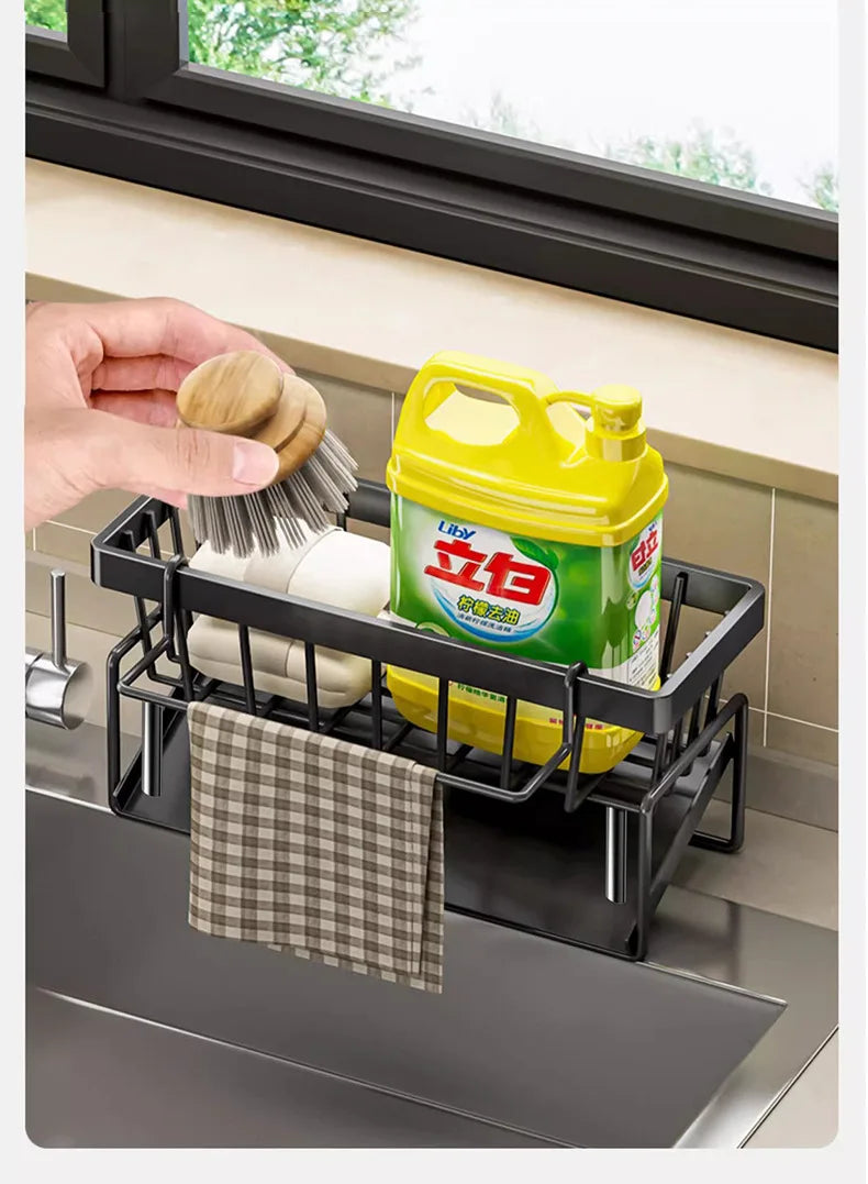 A black kitchen sponge holder and drain rack with a hanging hook is shown next to a window sill.