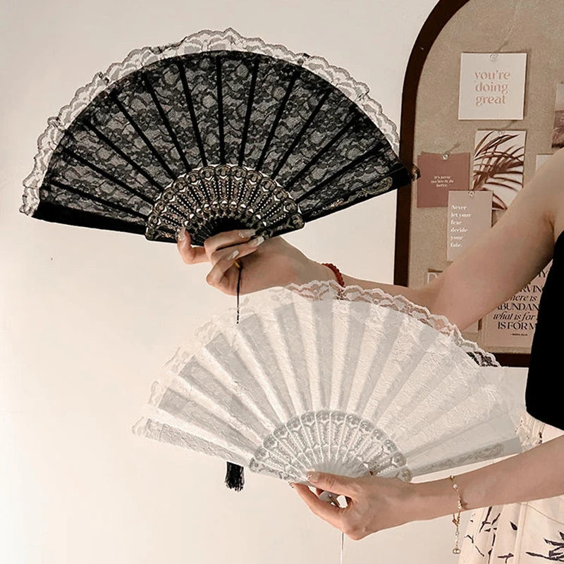 A person holds two folding hand fans, one black lace and one white sheer, against a light background.