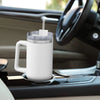 A white stainless steel travel tumbler mug with a lid is placed on a car console.