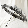 A black retro transparent folding umbrella with a floral pattern is shown open against a white background.