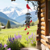 A red bird hangs from an ornate metal wind chime decoration near a wooden building with a scenic mountain view.