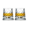 Un par de vasos de whisky facetados con líquido ámbar sobre bases de tono plateado.