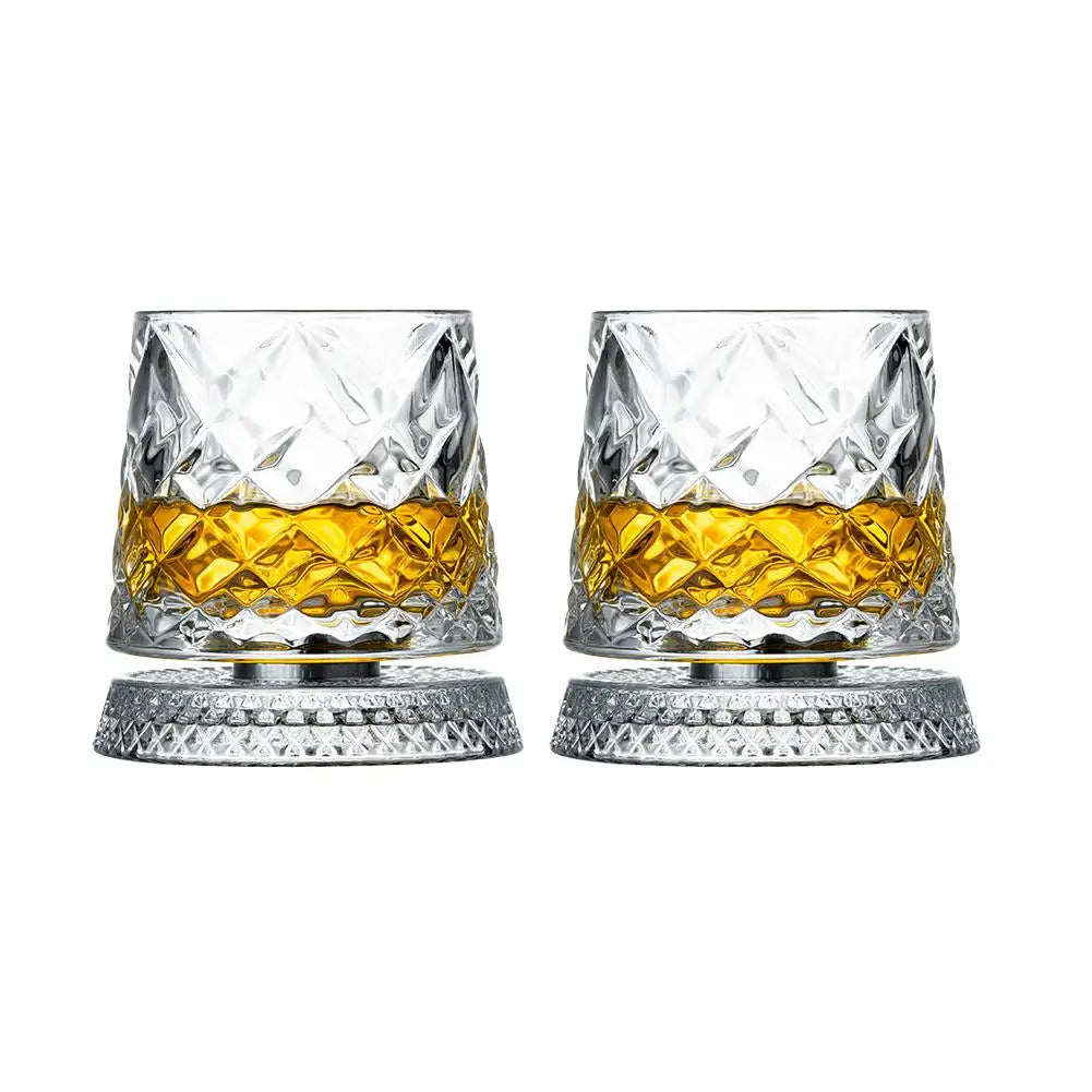 Un par de vasos de whisky facetados con líquido ámbar sobre bases de tono plateado.