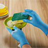 Hands in blue nitrile gloves are using a green sponge to clean a yellow dish.