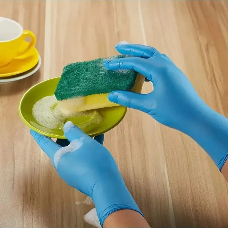 Hands in blue nitrile gloves are using a green sponge to clean a yellow dish.