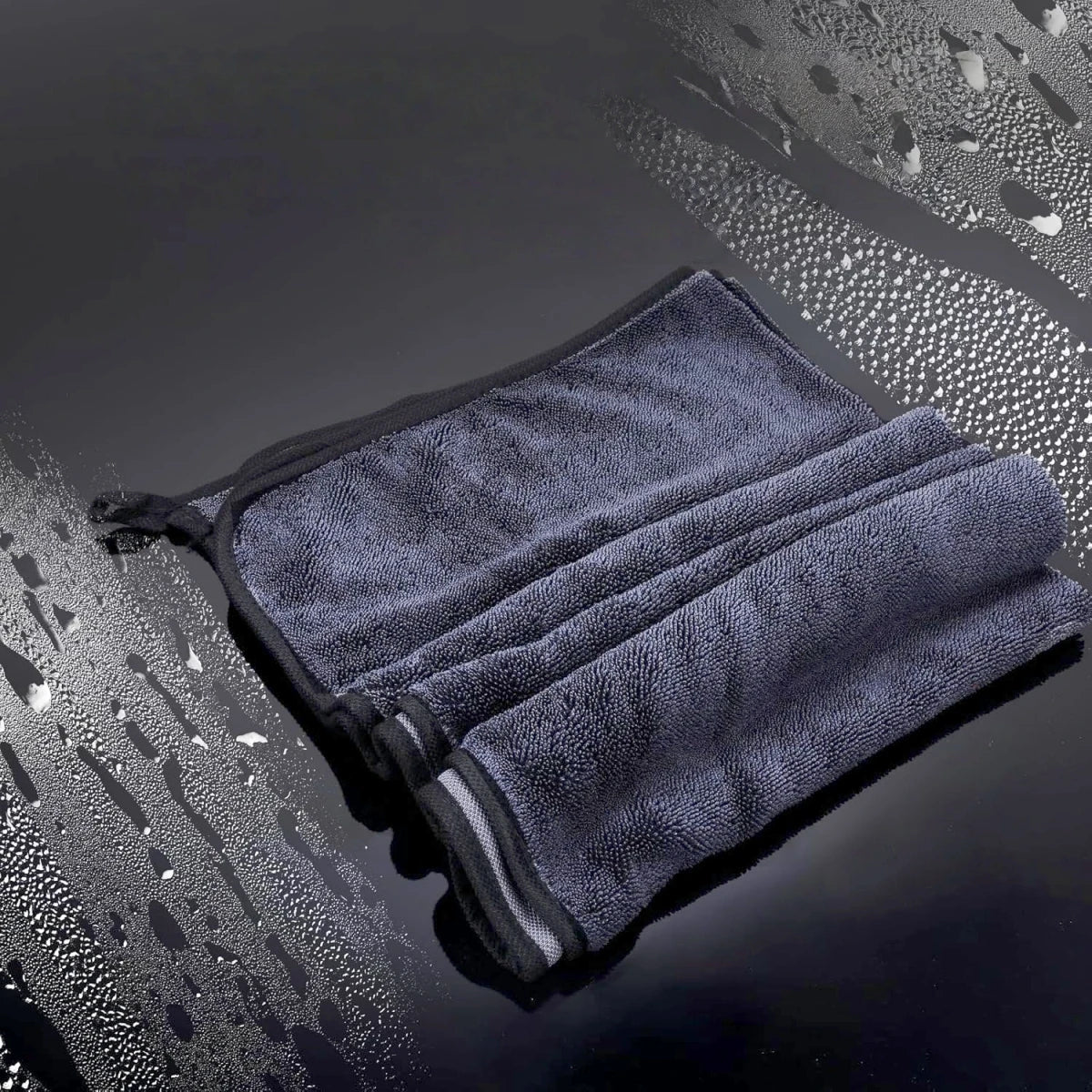 A dark gray microfiber drying towel is folded and placed on a wet, reflective surface.