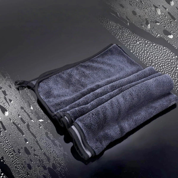 A dark gray microfiber drying towel is folded and placed on a wet, reflective surface.