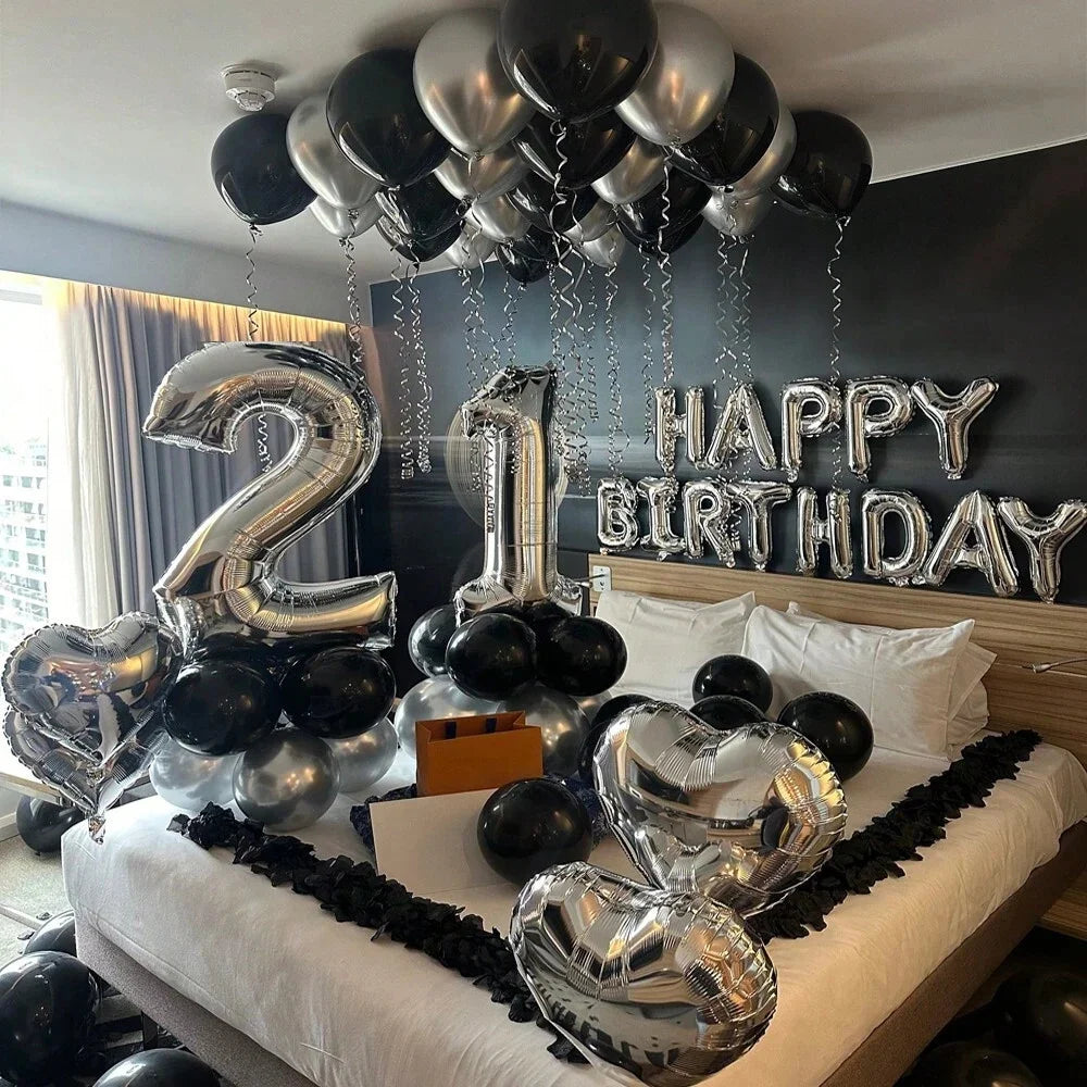 Silver and black balloons in various shapes including numbers, letters, and hearts decorating a party backdrop