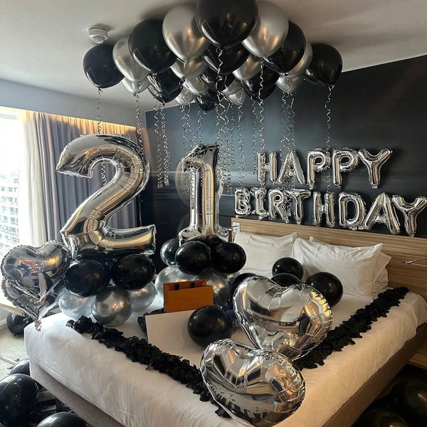 Silver and black balloons in various shapes including numbers, letters, and hearts decorating a party backdrop