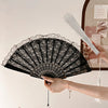 A hand is holding a black lace folding fan with a decorative edge and a white fan blade.