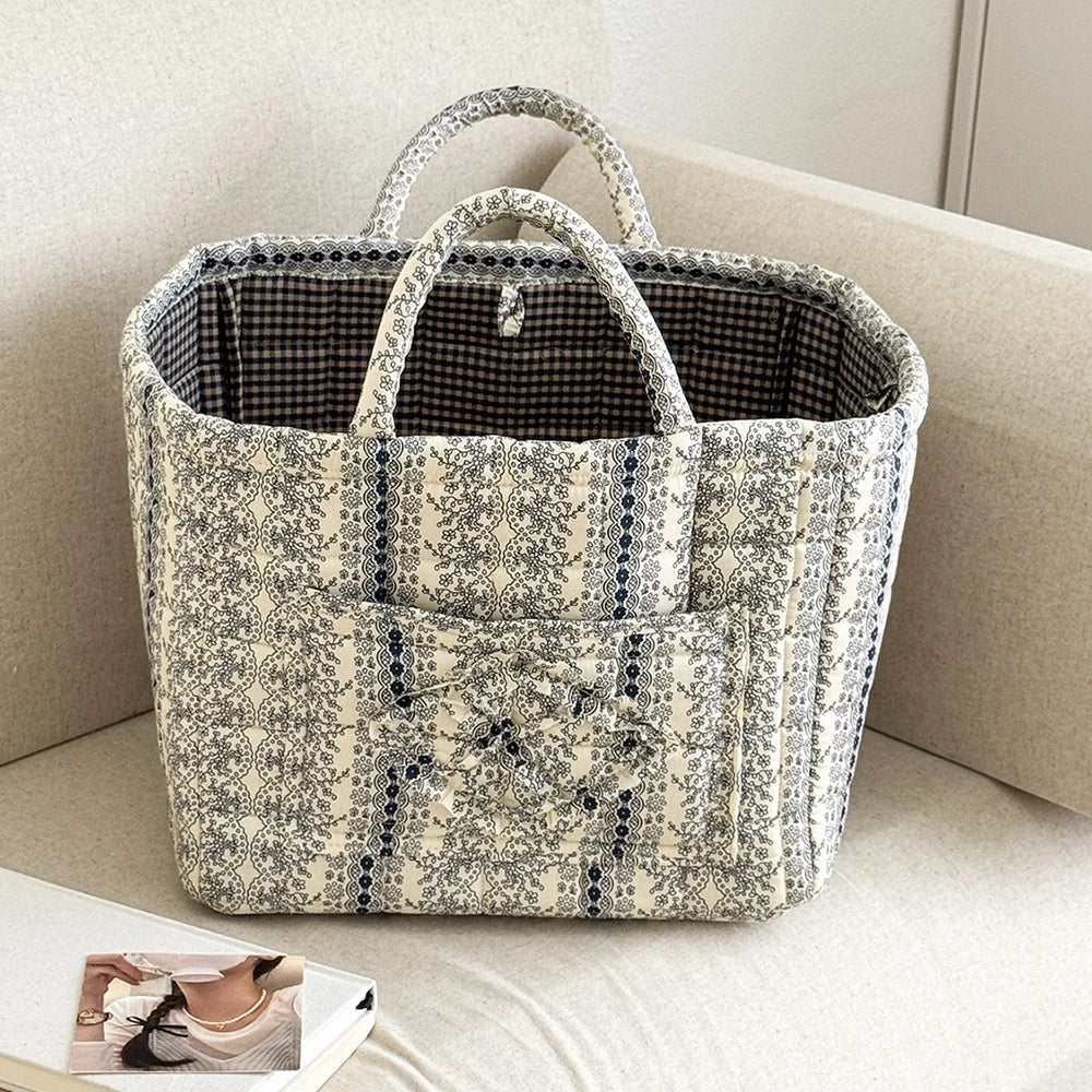 A beige and gray vintage floral storage basket with a handle sitting on a light-colored surface.