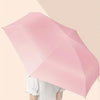A pink folding umbrella is held by a person, demonstrating its compact and expanded size.