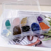 A clear plastic box holds a set of colorful natural crystal stones for energy and balance.