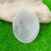 A smooth, translucent quartz thumb stone resting on vibrant green grass.
