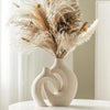 A dried floral arrangement in a beige ceramic vase on a white surface.