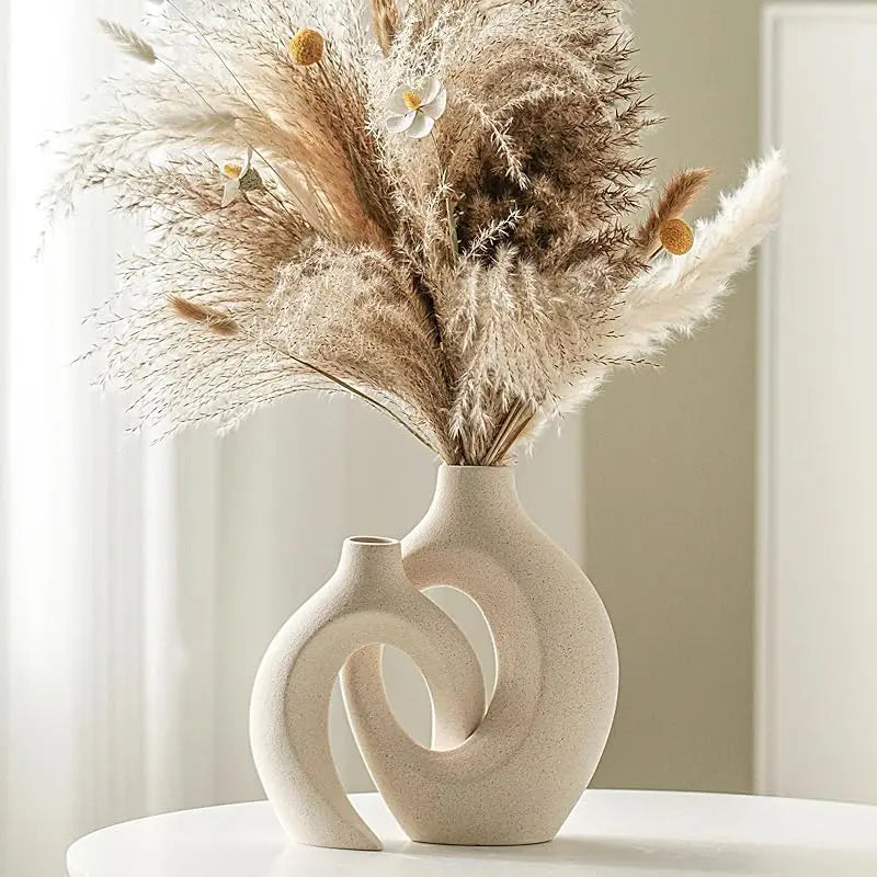 A dried floral arrangement in a beige ceramic vase on a white surface.