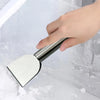 A hand is using a stainless steel multi-purpose scraper to clean ice or snow from a surface.