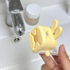 A yellow silicone faucet extender shaped like a cute rabbit is held by a hand next to a glass and a white bottle.