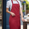 A woman wearing a maroon chef apron over a white t-shirt standing in an outdoor setting.