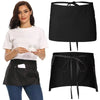 A woman models a black short apron with pockets, showing the front view of the garment.