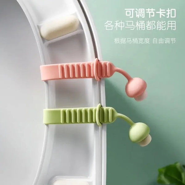 Extractor de tapa del inodoro de silicona en colores rosa y verde sobre un asiento de inodoro blanco.