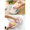 A hand is using a thickened washboard to gently wash laundry in a basin.