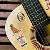 Close-up of a guitar body featuring stickers of golden retriever dogs and the text mom