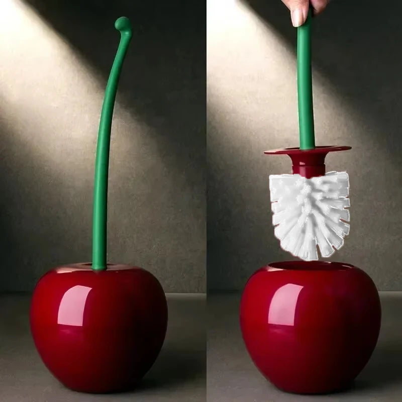 A hand holds a green toilet brush with a white head over a glossy red cherry-shaped base.
