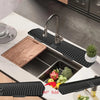 A black silicone kitchen sink drain mat with a 90-degree fold shown next to fresh vegetables.