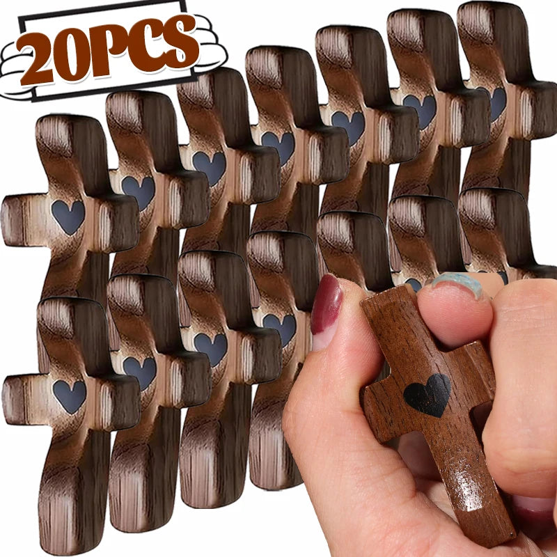 Une main tient un petit ornement de croix en bois gravé d'un cœur.