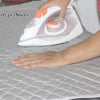 A hand is using a white folding ironing mat with orange accents to press a flat surface.