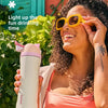 A woman holds an Owala insulated water bottle outdoors, smiling and wearing sunglasses.