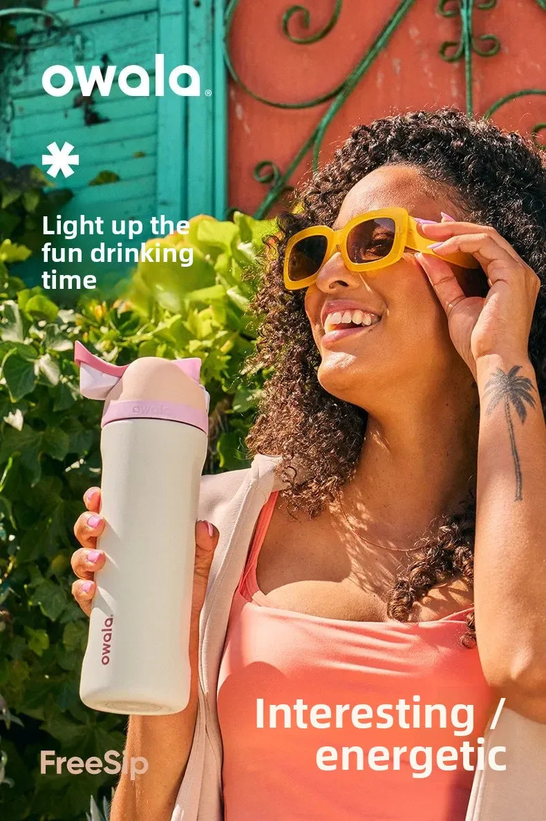A woman holds an Owala insulated water bottle outdoors, smiling and wearing sunglasses.