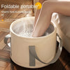 A person is soaking their feet in a portable folding foot soak tub made of light beige material.