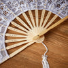 A light wood folding hand fan with delicate perforations is shown against a background of white lace fabric.