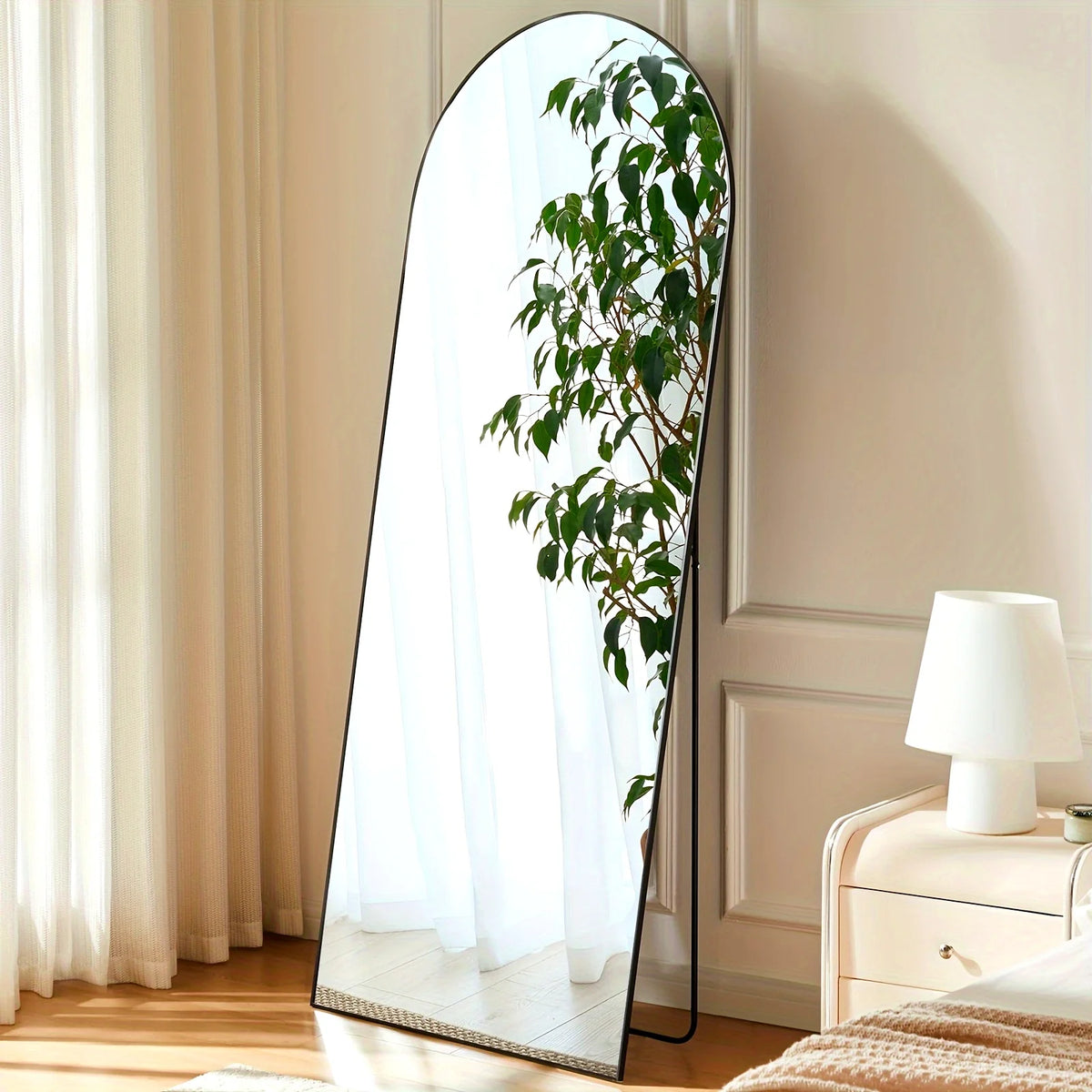 Full length arch mirror with an aluminum frame reflecting a leafy green plant in a bright room.