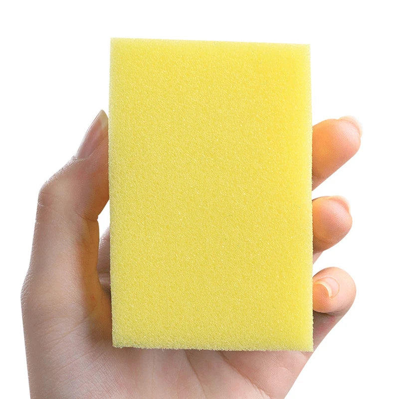 A hand holds a bright yellow double-sided scouring sponge.
