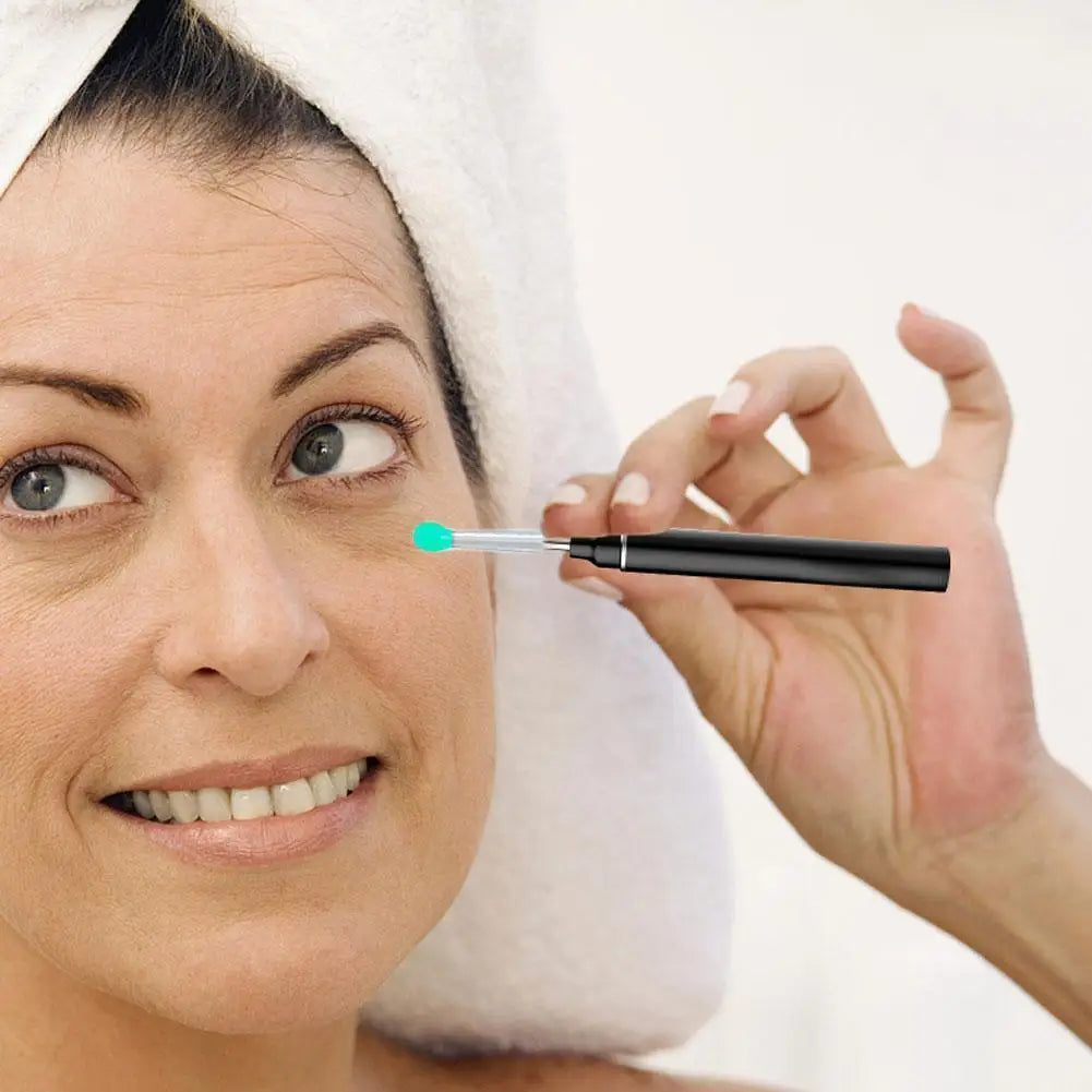A woman holds a thin, light blue replacement ear spoon near her eye while a white towel is visible.