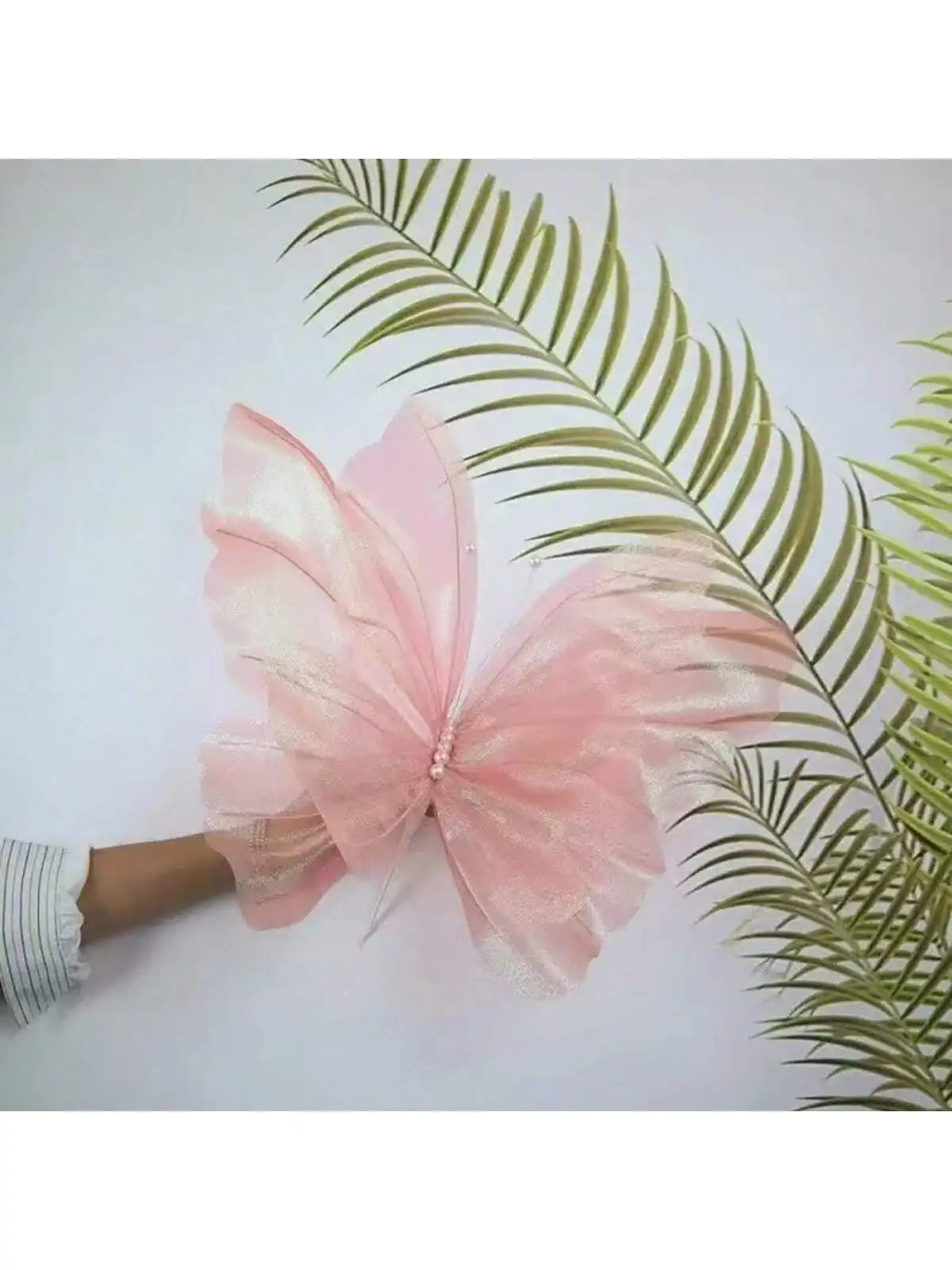 Pink glittery 3D simulated butterfly decoration resting on a green palm leaf.