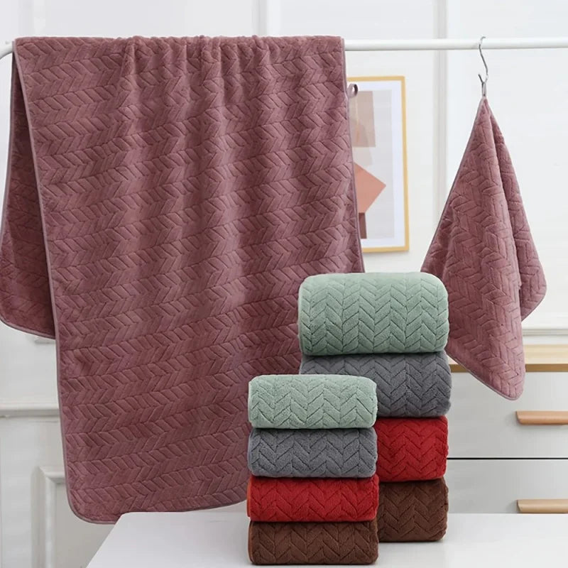A stack of soft coral velvet bath towels in various shades of pink and green on a white surface.