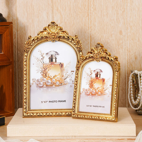 A pair of ornate golden arch photo frames displaying perfume bottles on a light wooden surface.