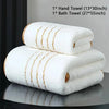 A stack of white hand and bath towels with gold stripes displayed on a dark surface.