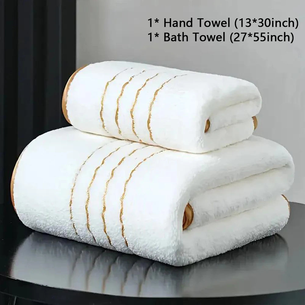 A stack of white hand and bath towels with gold stripes displayed on a dark surface.