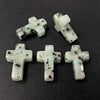Four natural agate and jasper cross pendant charms are displayed on a dark surface.